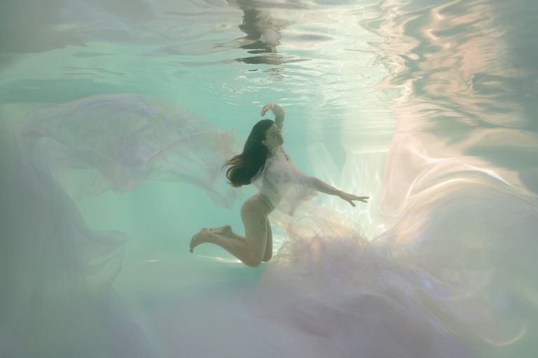 Dreamy underwater portrait with flowing pastel fabrics and soft light by White Lavender Photography, fine art photographer in Flower Mound, Texas.