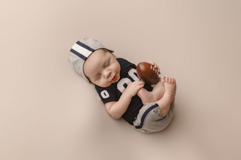 Luxury newborn session for Dallas Cowboys player – baby boy with football props in studio