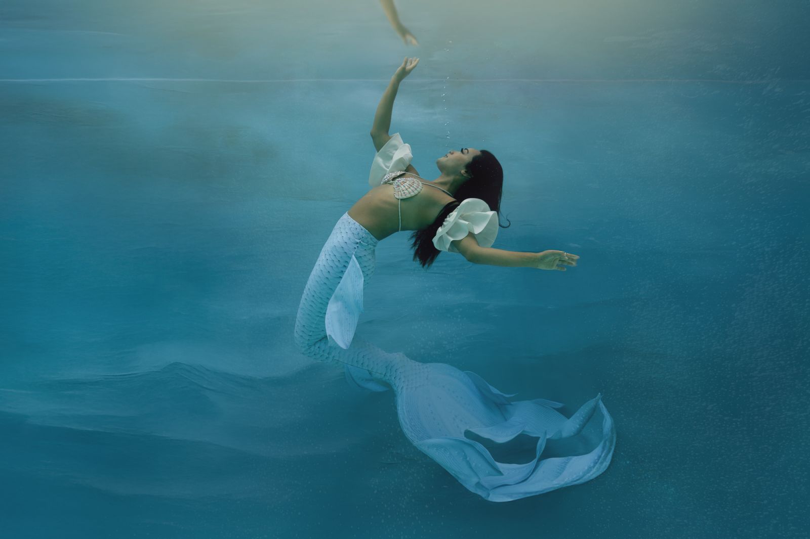 Luxury underwater mermaid photography featuring a woman reaching toward the surface, by White Lavender Photography in Dallas, TX
