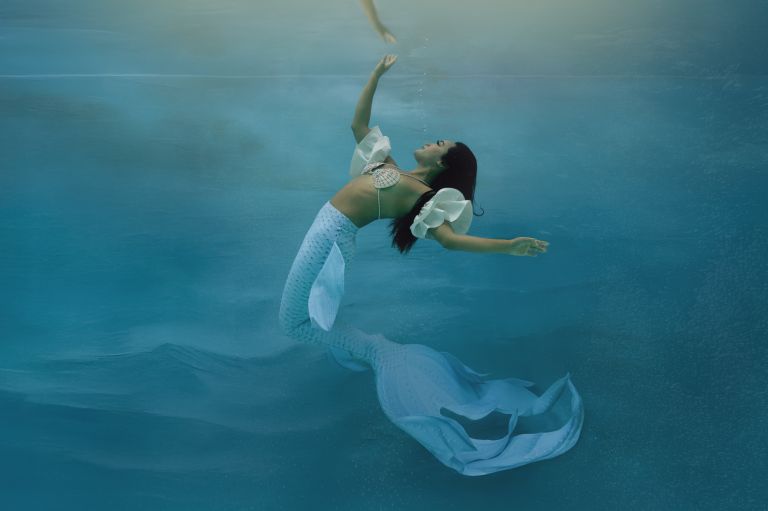 Luxury underwater mermaid photography featuring a woman reaching toward the surface, by White Lavender Photography in Dallas, TX