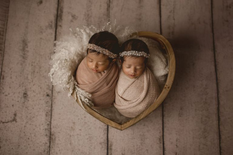 Newborn twins resting peacefully in a heart shaped prop during a relaxed studio photography session